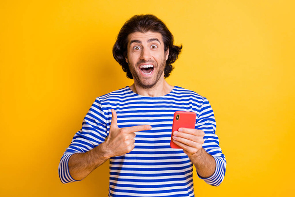 Photo of surprised crazy man point finger smartphone wear blue white vest isolated over bright yellow color background - Foto, imagen