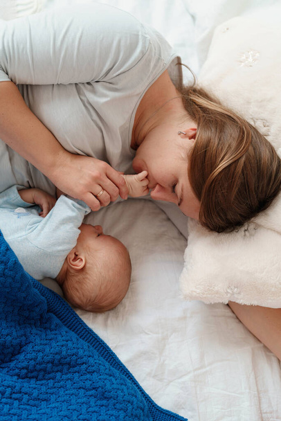 happy young woman feeds breast milk and hugs baby. a mother is breastfeeding a newborn baby while lying on the bed. Concept of newborn lactation. The child eats milk before going to bed. Side view. - Foto, Imagem