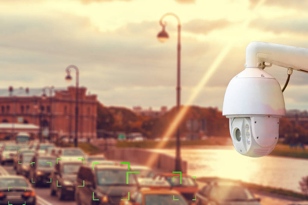 The concept of video surveillance and security technology. CCTV camera on the background of a road bridge with traffic in cloudy weather with a Sunny sunset. - Photo, Image
