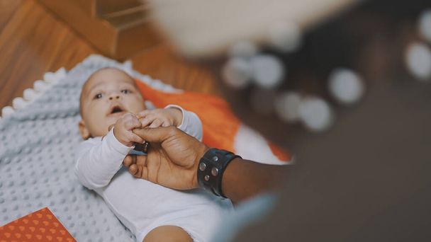 Adorable baby holding father hand. Mulatto baby playing with fathers hand. close up - Fotografie, Obrázek