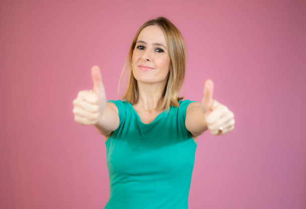 Smiling pretty young woman showing thumbs up isolated over pink background - Foto, afbeelding