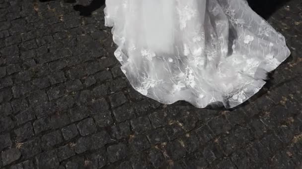 Casal amoroso de noiva e noivo em seu dia do casamento andar em vestido de noiva luxuoso e terno no pavimento da cidade e de mãos dadas - Filmagem, Vídeo