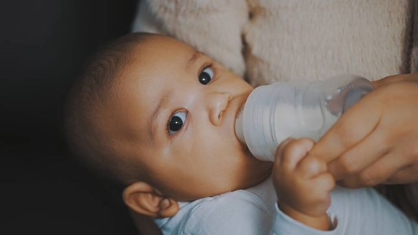 Close up adorável pele escura bebê bebendo seu leite da garrafa em mãos mães - Foto, Imagem