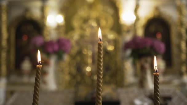 Tres velas de cera amarilla retorcidas en un soporte en espiral en la iglesia sobre un fondo borroso del altar y arden brillantemente - Metraje, vídeo
