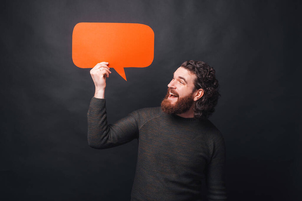 Photo of cheerful man in casual holding empty speech bubble and looking - Fotoğraf, Görsel
