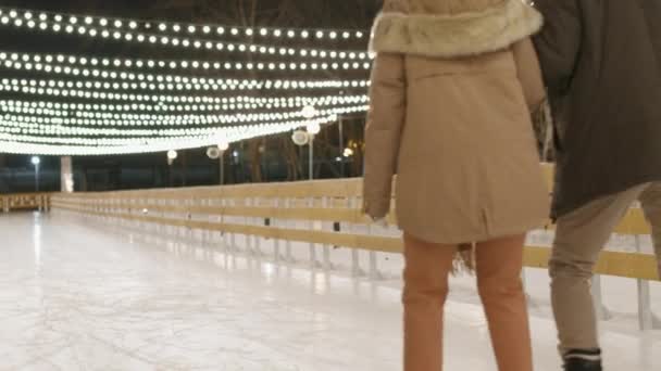 Volledige backview beelden van volwassen echtpaar in winterkleding schaatsen op lege ijsbaan buiten op koude winteravond - Video