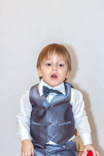 A little boy holds and hands over a red box, a Valentine's Day theme concept. Portrait of a cute boy in a suit with a bow tie. Valentine's Day. - Foto, Bild