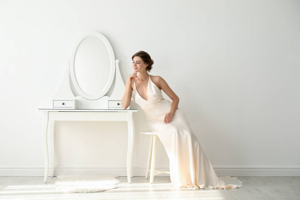 Young bride in beautiful wedding dress near mirror indoors - Foto, afbeelding