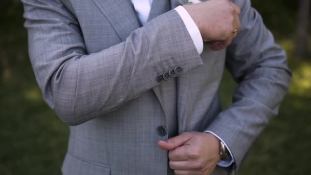 Un uomo caucasico con una fede nuziale sul braccio in un abito grigio e giubbotto e un papillon intorno al collo si alza e raddrizza le tasche nella giacca - Filmati, video