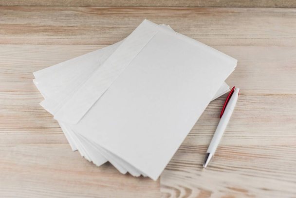 kantoorpost: een pakje witte lege enveloppen voor brieven, witte balpen ligt op een lichte houten tafel rechts - Foto, afbeelding