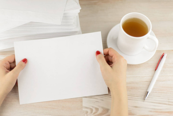 office routine: the office worker considers the form of the envelope for sending, waiting until cool fresh hot tea in a mug. A pile of empty envelopes lying behind. - Photo, Image