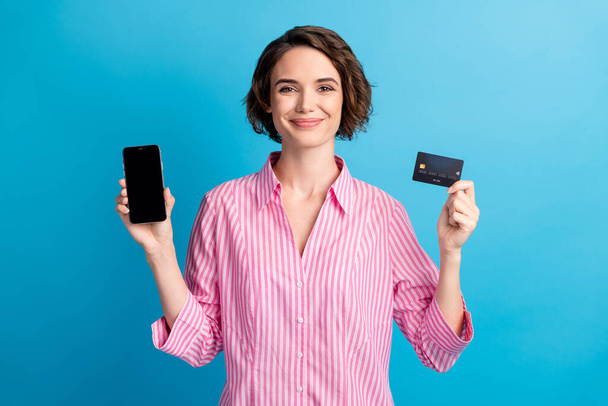 Photo of positive lady hold smartphone credit card easy pay wear pink white formalwear shirt isolated over blue color background - 写真・画像