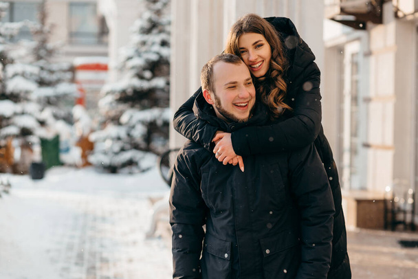 Una pareja amorosa en un suave abrazo en el fondo de una ciudad nevada - Foto, Imagen