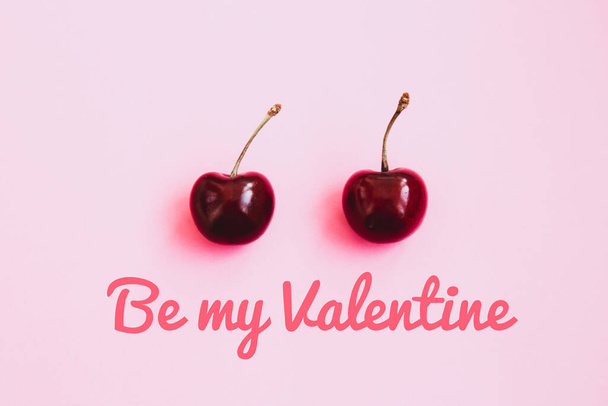 Two ripe cherries on a light pink background. Valentine's Day concept. Inscription Be my Valentine - Zdjęcie, obraz