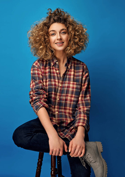 Young smiling woman with blonde curly hair wear cotton check shirt isolated on blue background - Photo, image