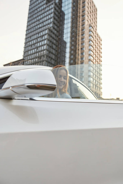 Smiling young caucasian girl getting in luxury car on street - Photo, Image