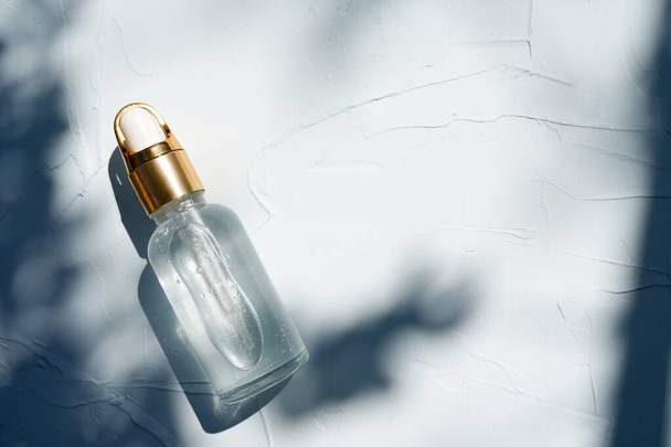 Концепция натуральной косметики, эфирное масло в стеклянной бутылке на бетонном фоне с тенью - Фото, изображение