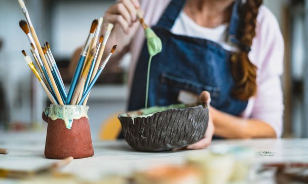 Woman mixing paint with brush inside ceramic bowl in workshop studio - Artisan work and creative craft concept - Photo, Image