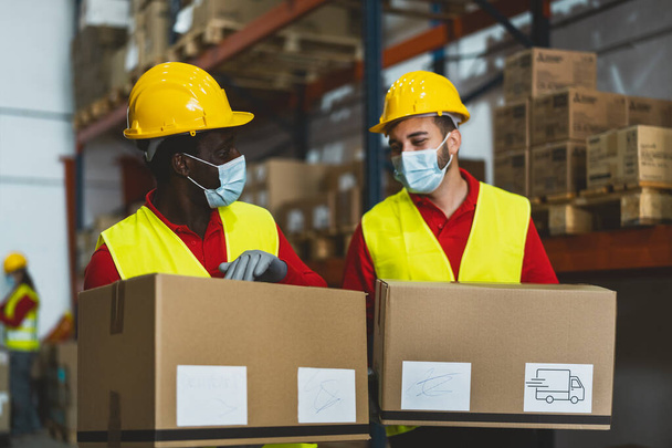 Команда, работающая на складе, загружая коробки доставки во время ношения маски для лица во время пандемии коронного вируса - Логистическая и промышленная концепция - Фото, изображение