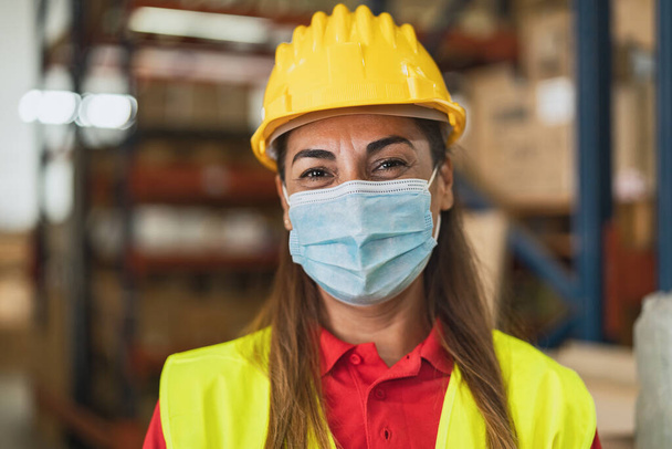 Mujer latina feliz trabajando en almacén mientras usa mascarilla facial durante pandemia de virus corona - Concepto logístico e industrial - Foto, Imagen