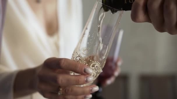 Im Urlaub hält ein junges weißes Mädchen ein transparentes, sauberes Glas in der Hand, das mit Perlen und einem eleganten Muster verziert ist, und eine andere Person schenkt Champagner mit schäumenden Blasen ein.. - Filmmaterial, Video