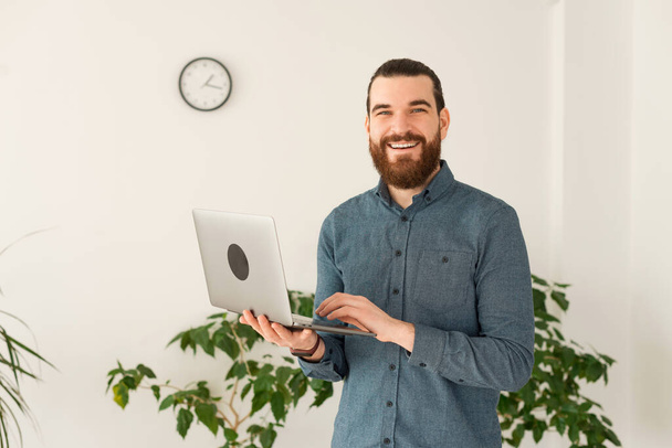 Portrét veselého kancelářského muže pracujícího na notebooku a usmívajícího se do kamery - Fotografie, Obrázek