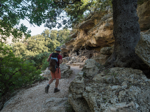 Man hiker at rocky hiking path to Cala Goloritze beach with limestone rocks, trees and green bush. Famous travel destination. Gulf of Orosei, Sardinia, Italy, September. - Photo, Image