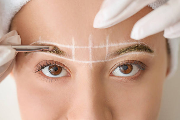 Young woman undergoing eyebrow correction procedure in beauty salon, closeup - Foto, afbeelding