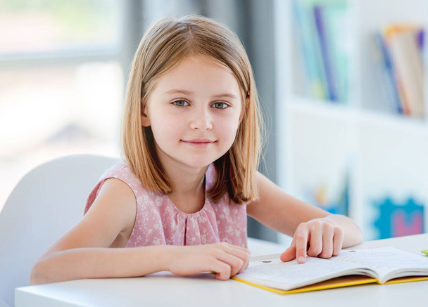 Schoolgirl with textbook sitting at desk - Foto, Bild