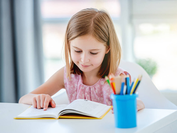 Little girl reading book in classroom - 写真・画像