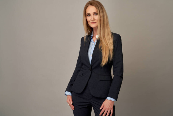 Portrait of adult woman with long blond hair posing in elegant suit over grey background in studio - Foto, imagen