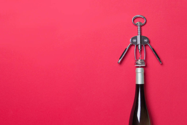 Flasche mit Weißwein und Korkenzieher auf rotem Hintergrund mit Kopierraum. - Foto, Bild