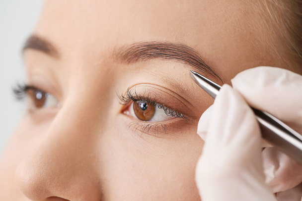 Young woman undergoing eyebrow correction procedure in beauty salon, closeup - Foto, Imagem
