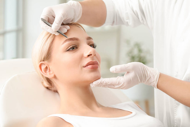 Young woman undergoing eyebrow correction procedure in beauty salon - Photo, Image