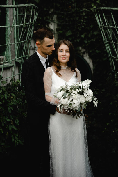 amazingly beautiful wedding couple stands in the ivy thickets. a beautiful young couple who started a family romantically walk through the botanical park. married people. wedding day. newlyweds on a background of greenery. - Photo, Image