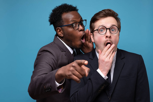 Afrikaanse man fluistert tegen zijn blanke collega oor vertelt hem geheim. - Foto, afbeelding