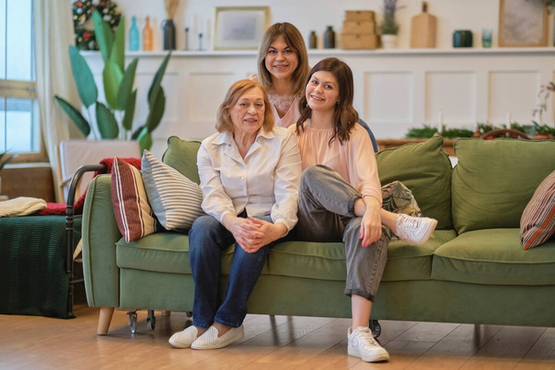 tre generazioni di una famiglia di donne sono sedute insieme sul divano. nonna, figlia e nipote posano insieme per ottenere una foto congiunta. - Foto, immagini