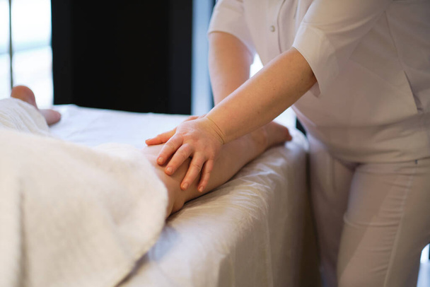 Деталь рук, що масажують м'яз людського теляти. Руки масажистки масажують ноги молодої жінки в спа-салоні. Догляд за тілом в спа-салоні для молодої жінки
. - Фото, зображення