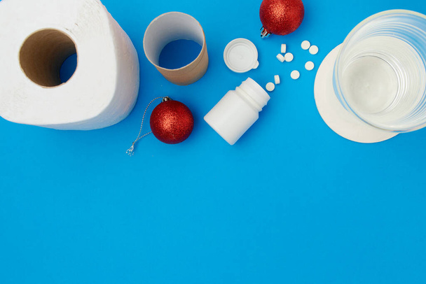 flat lay with christmas ball, toilet paper, pills and glass of water on blue background. - Zdjęcie, obraz