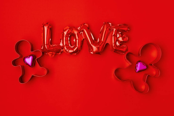 flat lay with gingerbread men cookie cutter couple, heart shaped candies and love inscription on red background. - Fotoğraf, Görsel