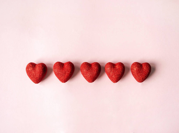 Cinco corazones rojos brillantes sobre un fondo rosa. Concepto de San Valentín. Vista superior. Copiar espacio. Enfoque selectivo - Foto, Imagen
