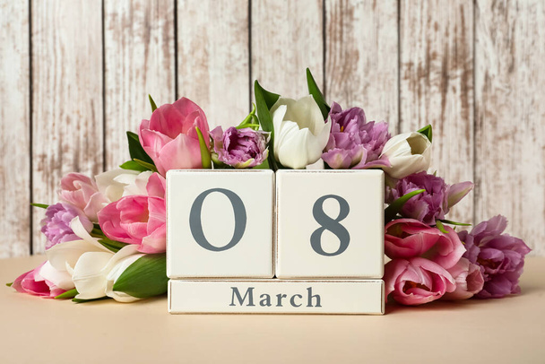 Block calendar with date 8th of March and tulips on table against wooden background. International Women's Day - Photo, image