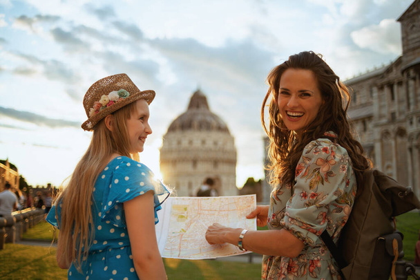 happy stylish mother and daughter with map and backpack enjoying promenade in square of miracles in Pisa, Italy. - Foto, imagen
