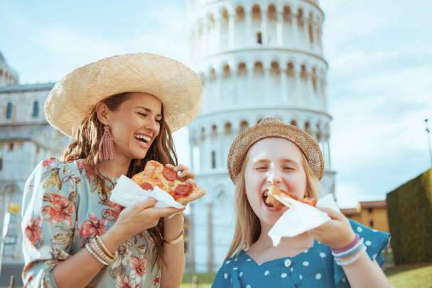 uśmiechnięta młoda matka i córka z pizzą w pobliżu Krzywej Wieży w Pizie, Włochy. - Zdjęcie, obraz