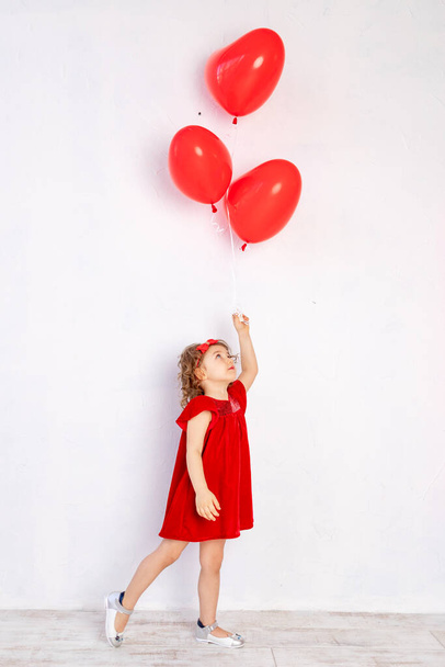 Дети Дня Святого Валентина. Маленькая девочка в красном платье держит шары в форме сердца - Фото, изображение