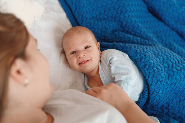 happy young woman lies and hugs the baby. a mother breast-feeds a newborn baby while lying on a bed. The concept of lactation of newborns. The child smiles and looks at the camera - Φωτογραφία, εικόνα
