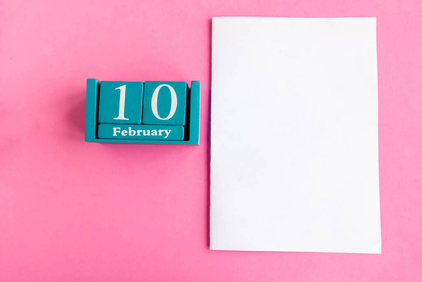 10 februari. Blauwe kubus kalender met maand en datum en witte mockup blanco op roze achtergrond.  - Foto, afbeelding