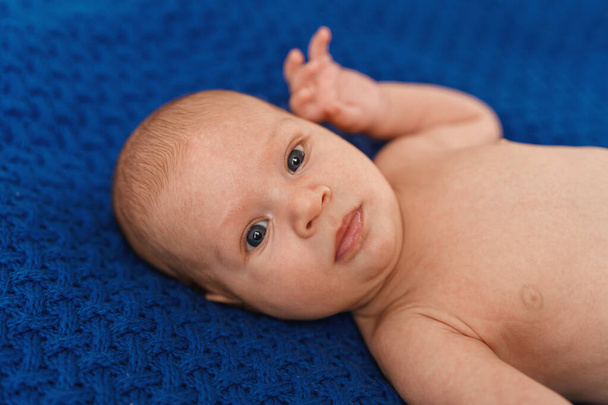 Cute 2-month-old blue-eyed Caucasian baby in a blue bodysuit is lying on his back on the bed, playing with his hands and looking into the frame. Close-up - Foto, Bild