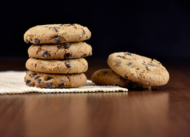 木製の背景ストック画像上のチョコレートチップクッキーの山.テーブルの上の甘いチョコレートクッキー。アメリカの甘いビスケット写真。テキスト用のコピースペースを持つ木製の背景にクッキー - 写真・画像