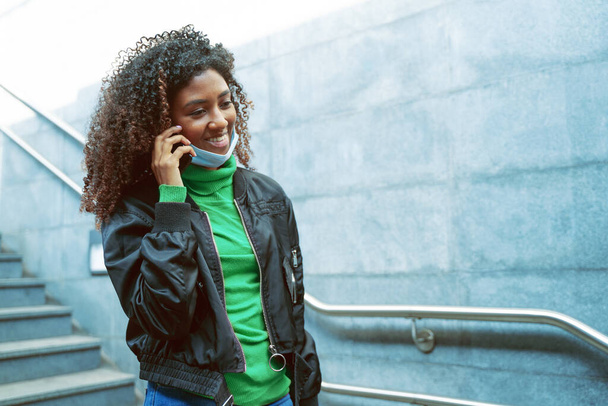 Musta nainen käyttää kasvonaamiota. Käytä matkapuhelinta kävellessäsi metrossa - Valokuva, kuva
